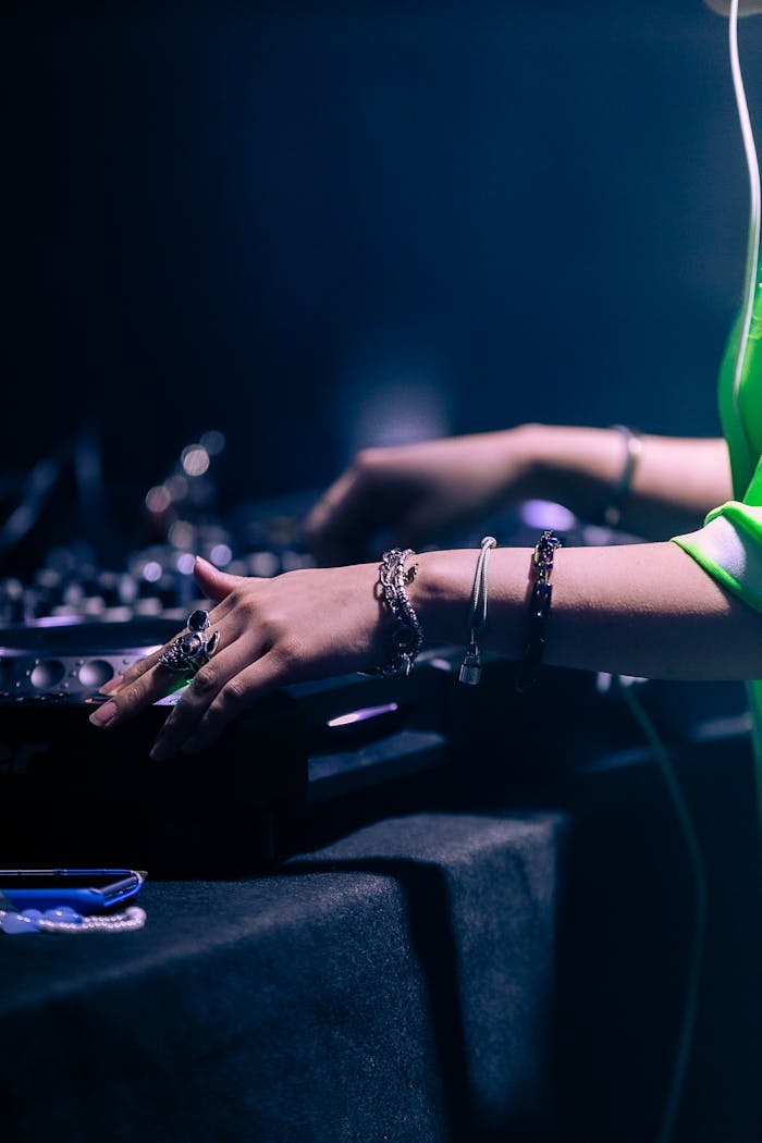 A DJs hands mixing electronic music on a controller at a vibrant nightclub party.